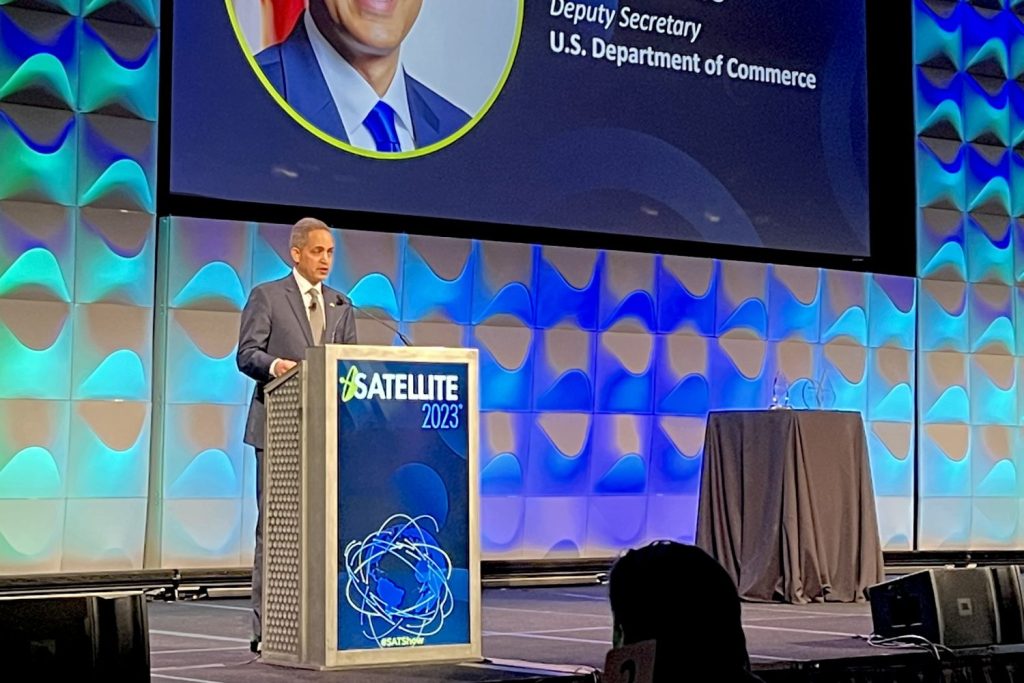 Deputy Secretary Don Graves standing at podium on stage with colorful backdrop and SATELLITE 2023 graphic